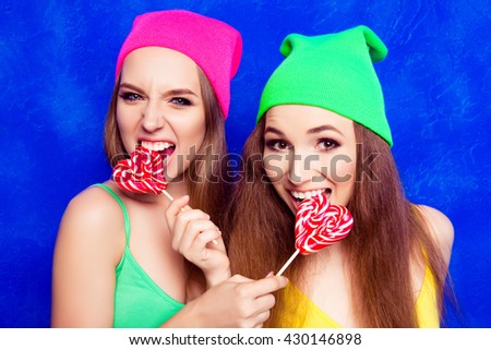 Portrait of attractive happy girls in hats biting lollipops