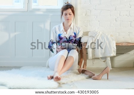 Young woman sitting on floor at home, using tablet computer.