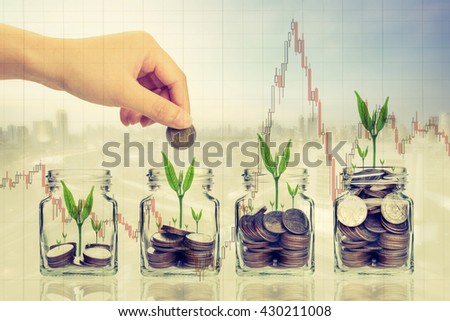 Hand putting money coins and seed in clear bottle on photo blurred cityscape background,Business investment growth concept.with stock chart.