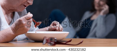 Panoramic picture of a senior woman eating a soup and her granddaughter talking on the phone in the background