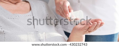 Panoramic picture of a nurse giving pills to a senior woman