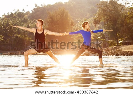Fitness, sport, and lifestyle concept - couple is exercising making yoga  at  tropical sunrise background.