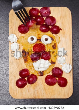 Funny looking face made of sliced grapes, strawberries and pancake, as seen from above