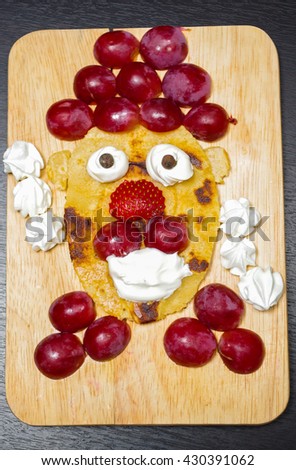 Funny looking face made of sliced grapes, strawberries and pancake, as seen from above
