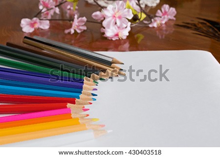 Colored drawing pencils and flowers in a variety of colors on white paper and wood background