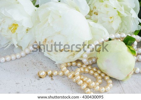 White fresh peony flowers with pearls jewellery on white wooden table