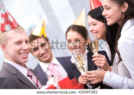 Image of happy man holding wrapped giftboxes with cheering friends on background