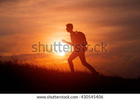 Silhouette of tourist man spread hand on top of a mountain enjoying sunset. Sport and active life concept