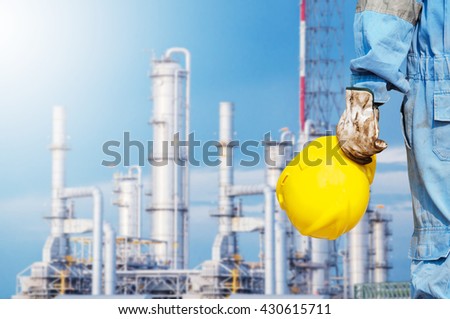 engineer hand holding yellow helmet for workers against background oil refinery distillation towers