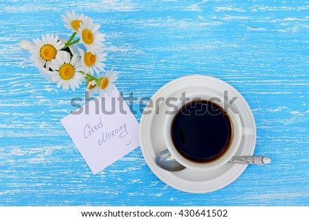 Daisy flowers and cup of tea with good morning note on rustic blue wooden background