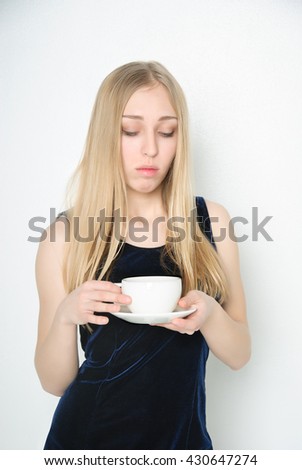Young lonely woman in dark-blue dress with mug of hot tea, feeling sad (on light background)