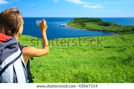 Young woman with backpack taking photo of a nature