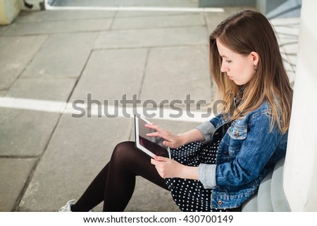Young girl sitting on the college campus yard studying with the tablet handheld device