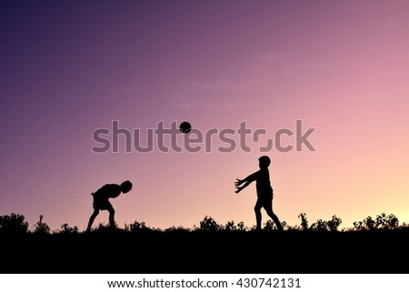 Silhouette children playing ball at sunset
