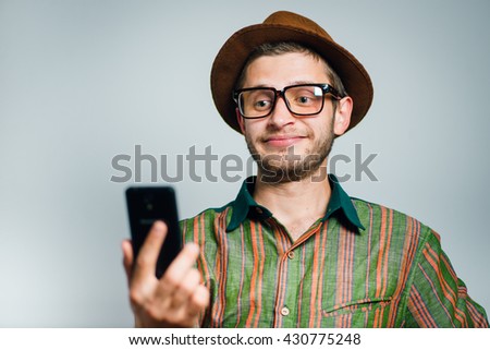 hipster man makes selfie photo on the phone, wearing a hat and glasses, isolated on a gray background