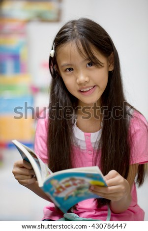 Little Asian child reading a book on the library