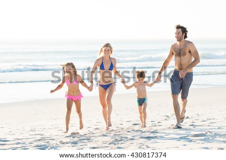 Smiling family running with holding hands at beach. Happy family having fun together on beautiful sunny beach. Young family on beach vacation.
