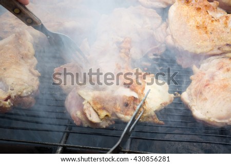 Turning over raw pork chops on grill. Smoke rising from heated grill