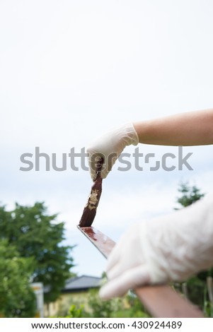 Active senior woman / girl / lady painting some pieces of wood / timber by brown paint colour with red brush and white gloves (color toned image)