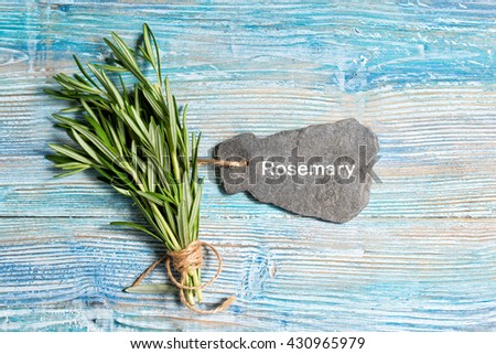 Fresh rosemary bunch with slate sign and text Rosemary on blue wooden background
