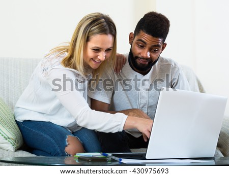 Happy smiling mixed young couple browsing web by laptop at home
