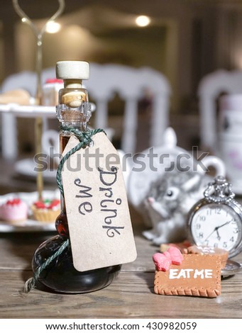 Magic Bottle with a tag that reads "drink me", Low key Photography Style. Abstract Blur of Mad Tea Party on the Background. Dark fairytales and Alice in Wonderland concept. 