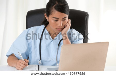 Thoughtful asian doctor looking at laptop with hand under her chin