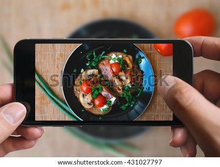 Taking picture of bacon sandwiches with tomatoes, mushrooms and cheese with mobile phone in male hands. Plate is on a bamboo mat. Vintage style.