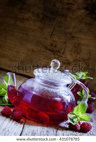 Red fruit and berry tea with raspberries in a glass teapot with mint on a vintage wooden background, selective focus