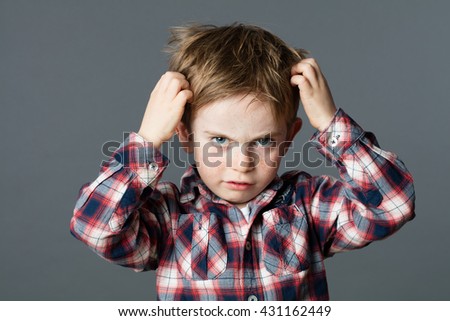 mischievous unhappy 6-year old kid with freckles scratching his hair for head lice or allergies, grey background studio
