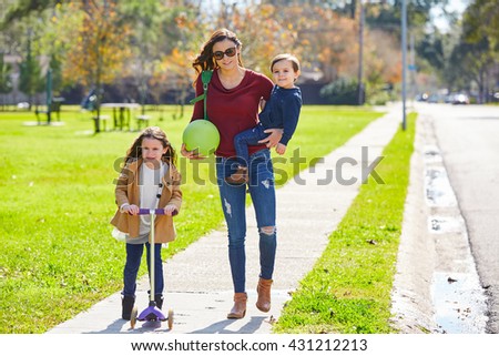Mother daughter and son family in the park walking with ball and skate scooter