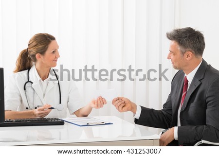 Female Doctor Giving Prescription Paper To Mature Businessman