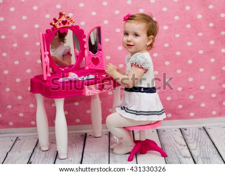 little girl on a pink background playing with a doll