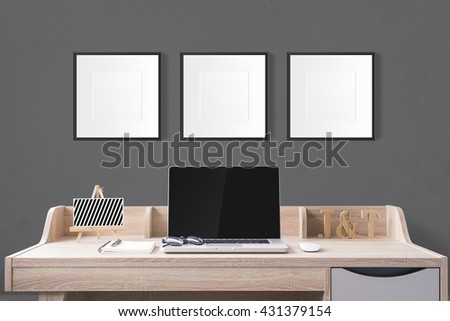 notebook computer and stationery on working table with blank photo frames in the studio with dark grey wall.