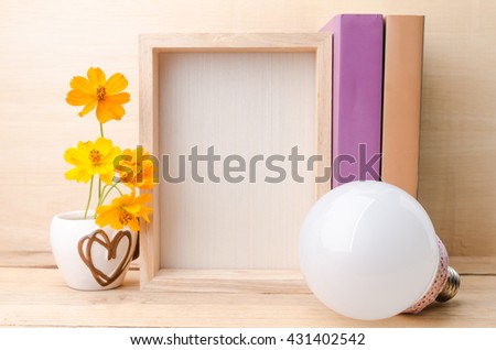 Photo frame with books, flowers and lamp on the wooden table