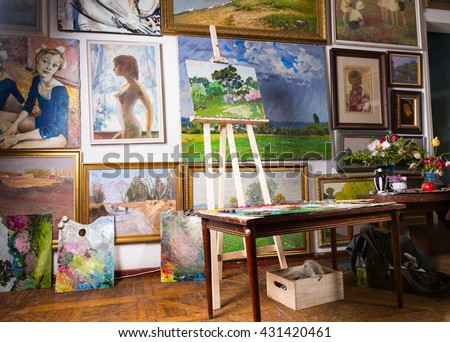 Interior of a painters studio or gallery with colorful canvases covering a variety of subjects hanging on the wall and an unfinished painting on a wooden easel