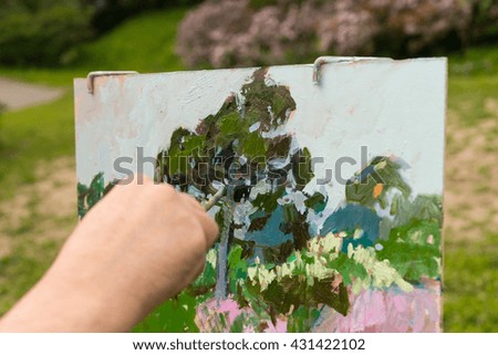Male hand of the painter holding  paintbrush and painting a garden scene with flowers outdoors
