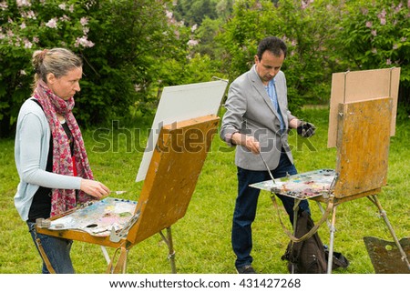 Two professional creative painters working  on a trestle and easel painting with oils and acrylics during an art class in a park