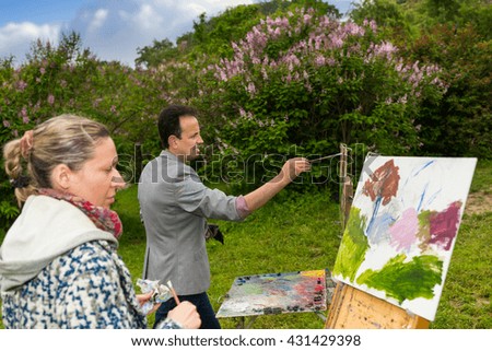 Serious couple of male and female artists in a process of painting with oils and acrylics during an art class in a park