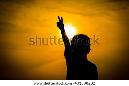 Abstract photo sunset orange evening light, a boy holds up two fingers as a sign of fighting with everything.
