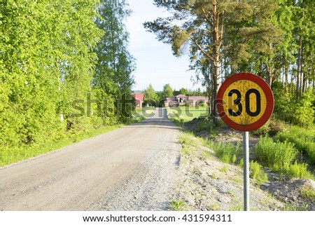Speed limit sign in the country side on a summer evening. The speed limit is 30 km/h on a gravel road. The focus point is on the speed limit sign on the right.