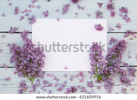 Lilac spring flowers with blank paper for greeting message on a light blue shabby wooden background. Vintage Floral mock up with purple flowers. Copy space