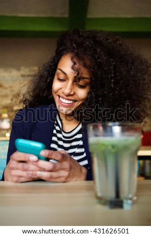 Close up portrait of smiling young woman reading text message on her mobile phone in coffee shop