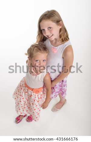 Wonderful siblings with big blue eyes and pleasant smiles. The elder sister embraces the youngest one. Full body shot from the upper angle.