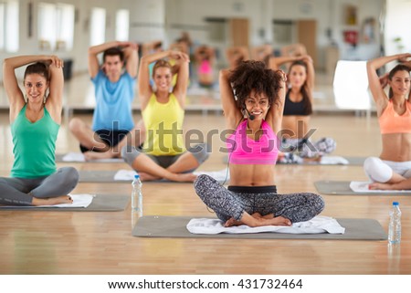 Young curly female instructor doing yoga exercises with group in gym