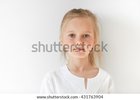 Portrait of angel-like child in white morning light in studio. Little European girl with blond hair looking attractive and balanced showing neutral emotions and radiating tranquility.