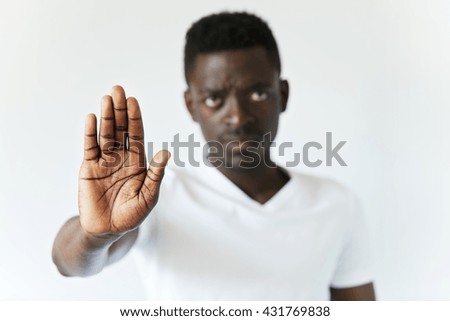 Isolated shot of serious African male showing stop sign with his open palm, saying that you better stay away from him. Young black man looking at the camera with unfriendly expression. Film effect Royalty-Free Stock Photo #431769838