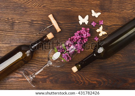 Wineglass with lilacs, bottles and butterflies decorations on the wooden background