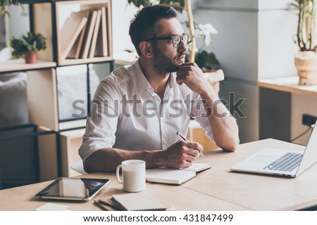 In search of inspiration. Thoughtful mature man holding pen and looking away while sitting at his working place in office  Royalty-Free Stock Photo #431847499