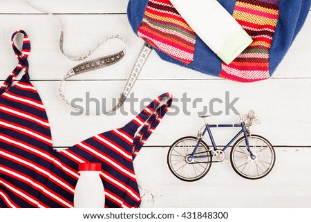 Travel and sport concept -  bicycle model, striped backpack, swimsuit, sunscreen, bottle of water and centimeter tape on white wooden desk